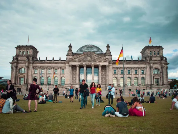 Auf der Wiese vor dem Bundestag in Berlin sitzen einige junge und ältere Menschen.